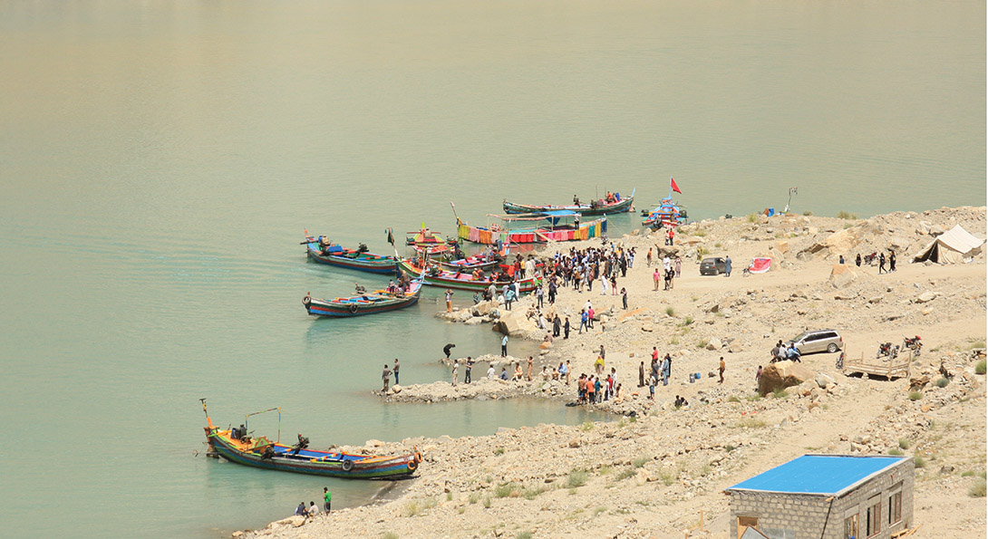 A photograph taken from above of people gathering on a beach. Six smaller boats