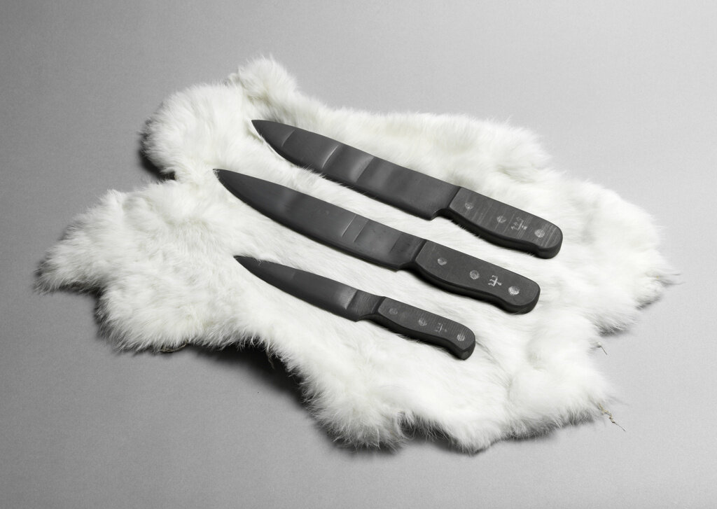 Three black knives in various sizes resting on a white fur against a gray background.|Black and white image of Lawrence Steger pressing his right hand gently against his cheek